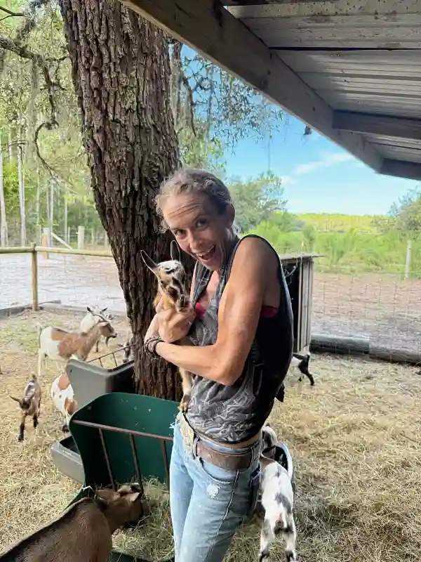 Woman smiling and holding baby goat with goats around