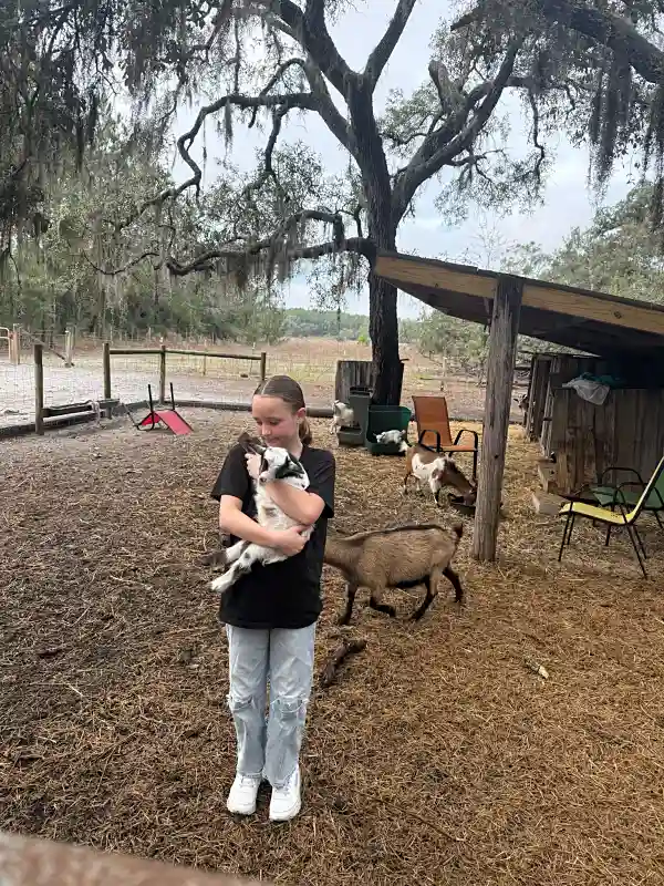 Girl holding baby goat with goats in background